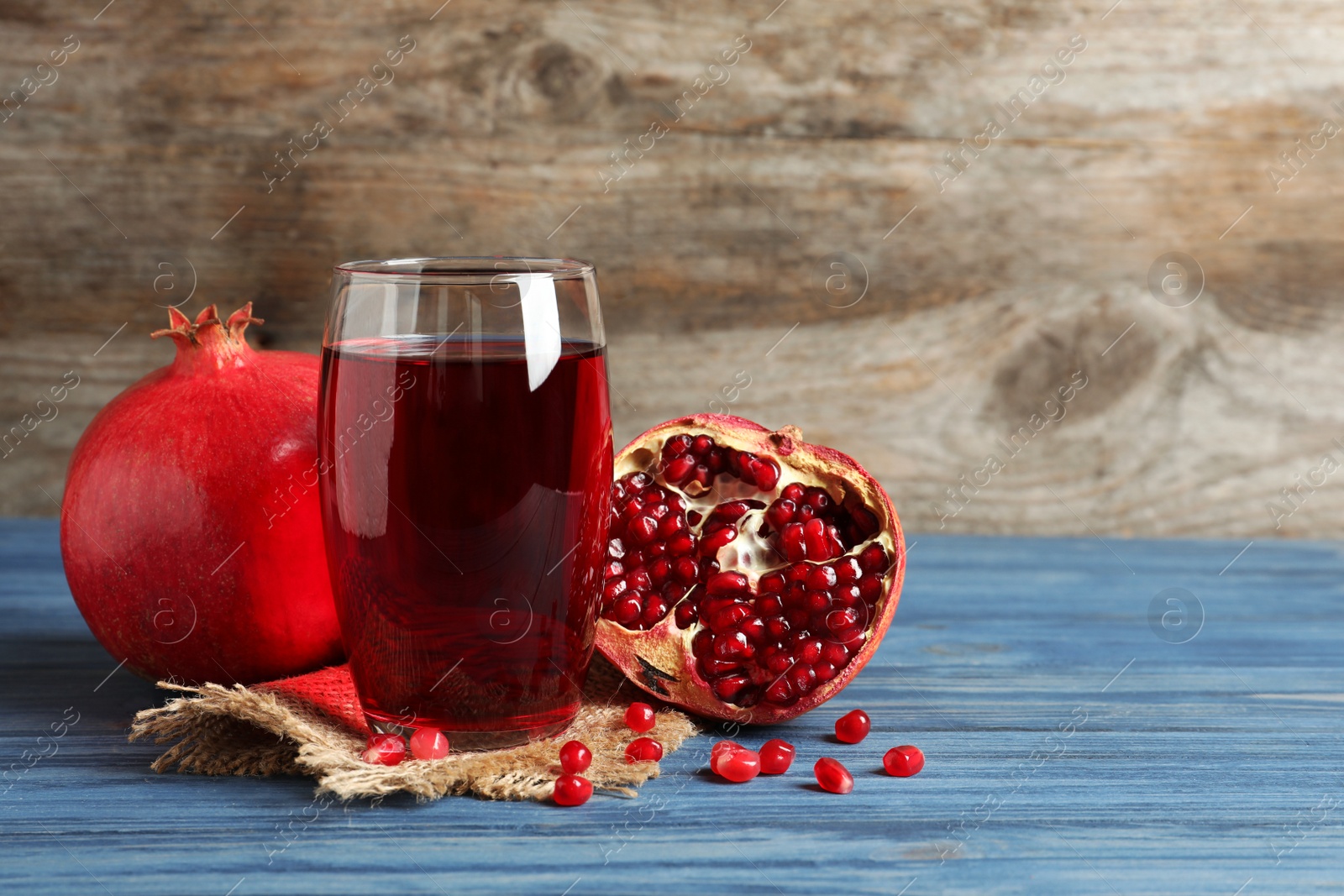 Photo of Glass of pomegranate juice and fresh fruits on table against wooden background, space for text