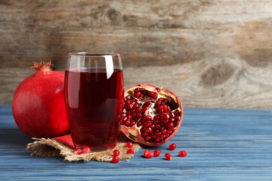 Photo of Glass of pomegranate juice and fresh fruits on table against wooden background, space for text