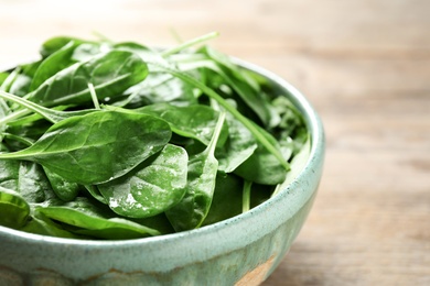 Photo of Bowl of fresh green healthy spinach on wooden table, closeup