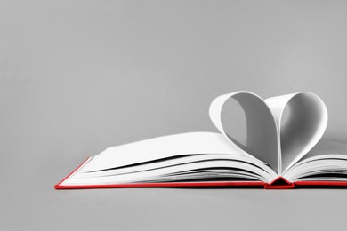 Photo of Open book with pages folded in heart on grey background, closeup. Space for text