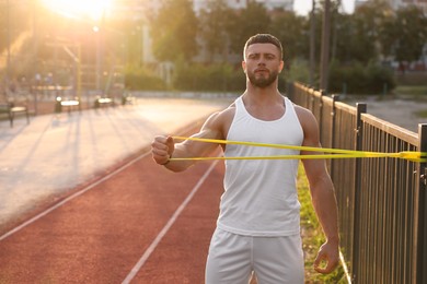 Muscular man doing exercise with elastic resistance band outdoors at sunset