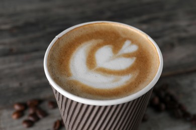 Coffee to go. Paper cup with tasty drink and roasted beans on wooden table, closeup
