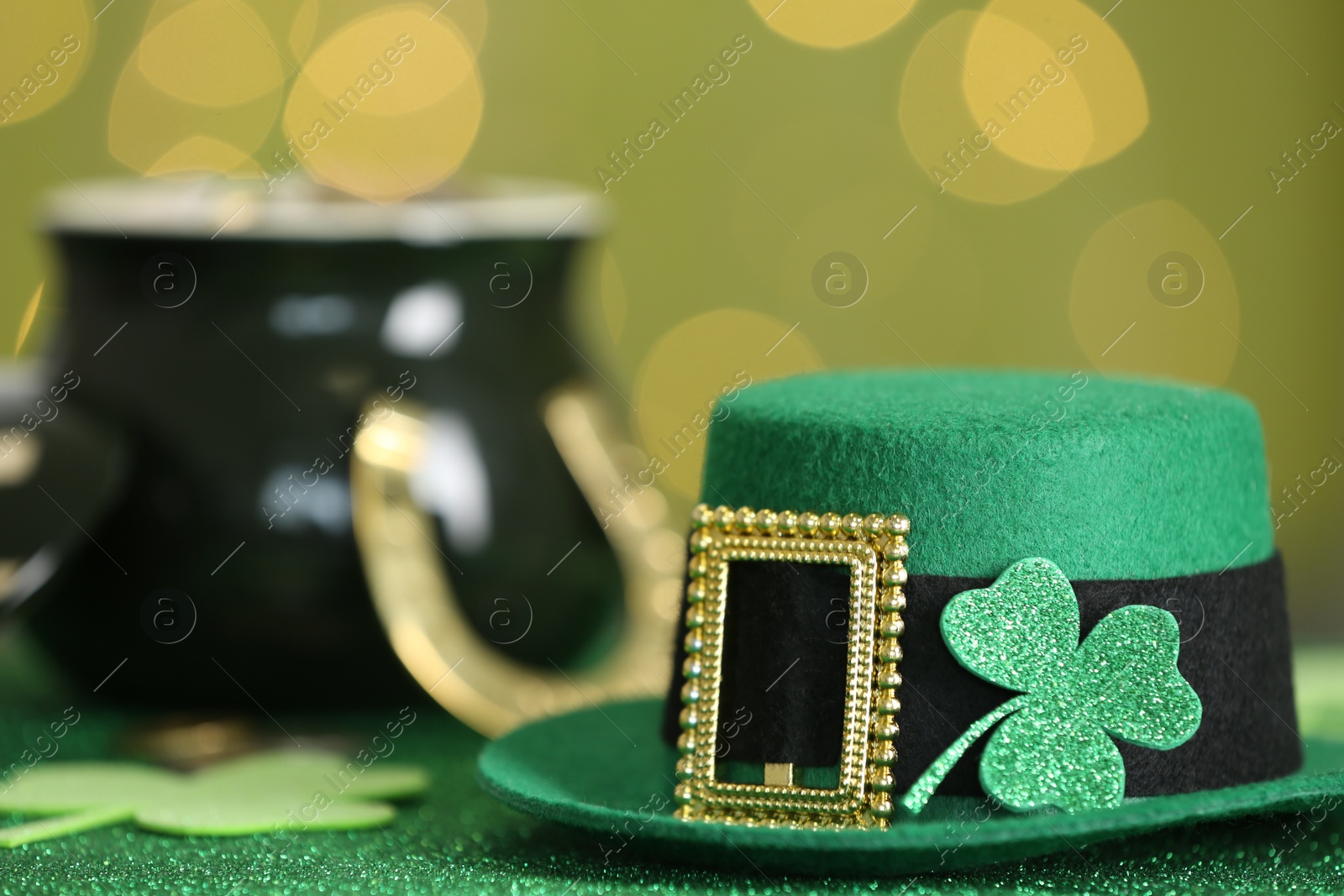 Photo of Leprechaun hat with clover leaf on table against blurred lights, space for text. St Patrick's Day celebration