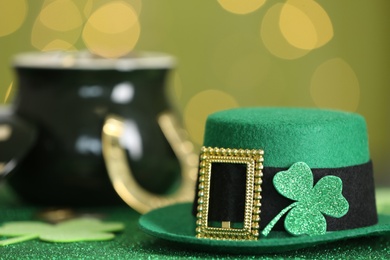 Leprechaun hat with clover leaf on table against blurred lights, space for text. St Patrick's Day celebration