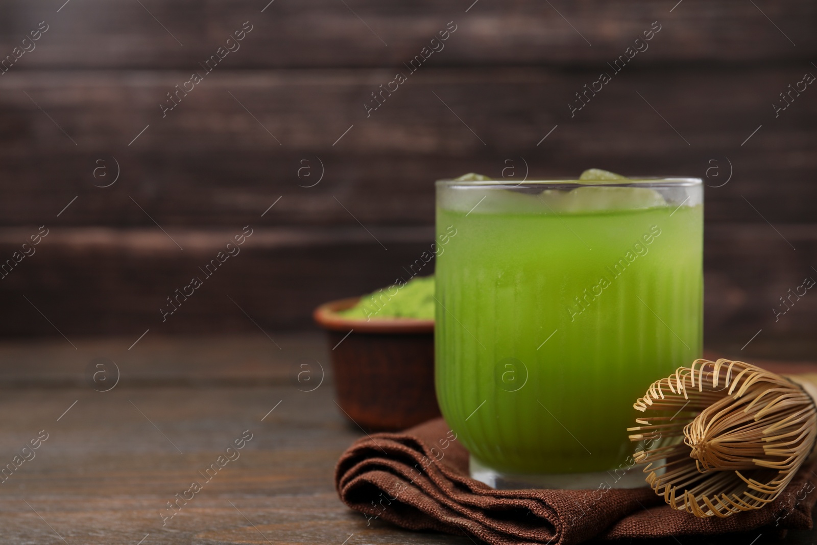 Photo of Glass of delicious iced green matcha tea and bamboo whisk on wooden table, closeup. Space for text