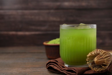 Glass of delicious iced green matcha tea and bamboo whisk on wooden table, closeup. Space for text