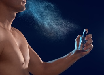 Photo of Young man spraying perfume on black background, closeup