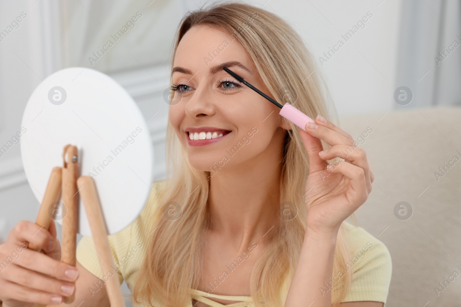 Photo of Beautiful woman with mirror applying mascara at home