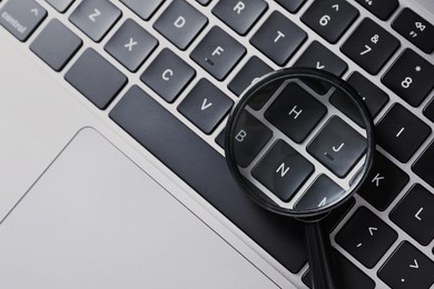 Photo of Magnifying glass on keyboard of laptop, top view