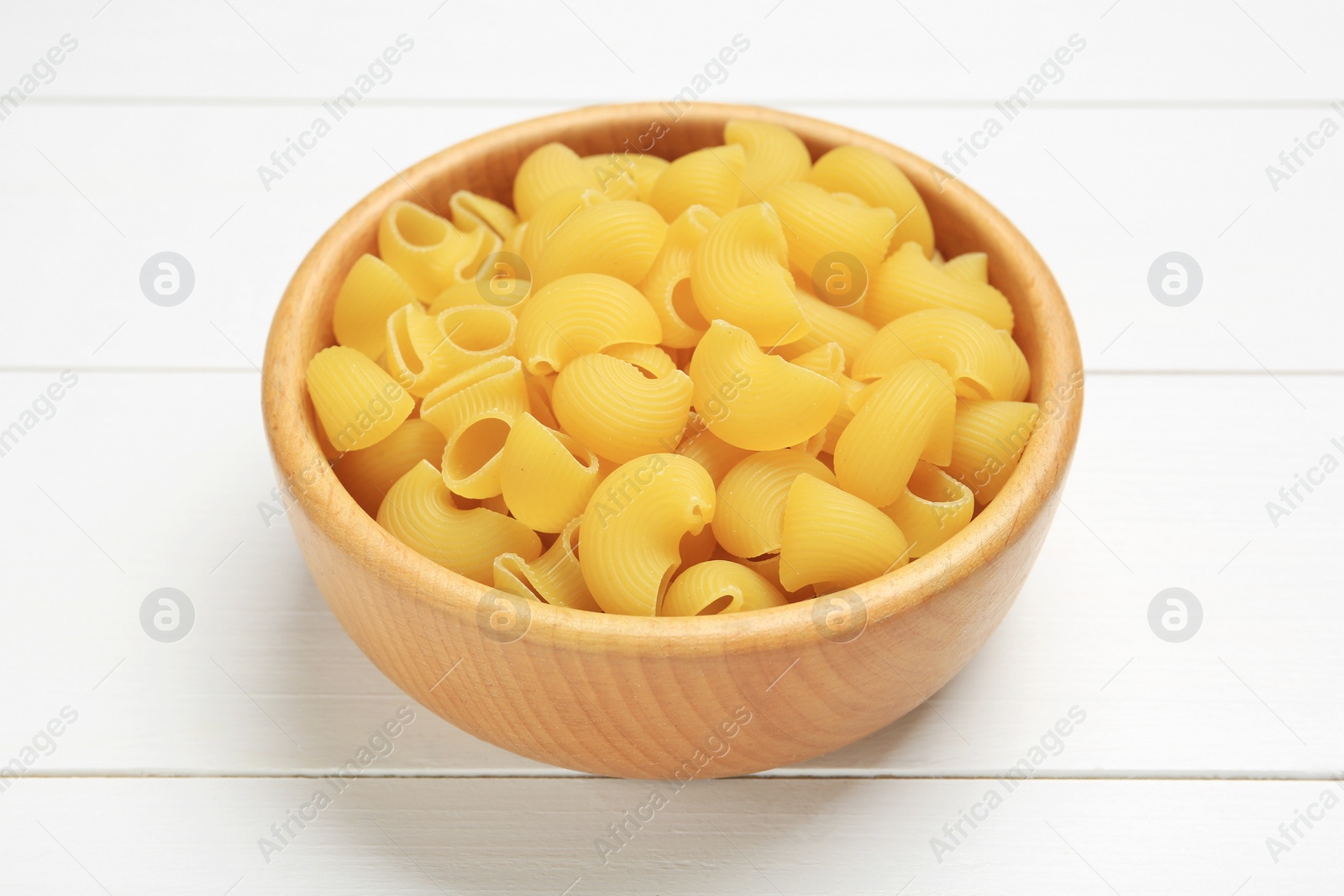 Photo of Raw macaroni pasta in bowl on white wooden table, closeup