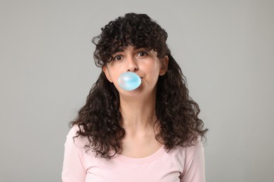 Photo of Beautiful young woman blowing bubble gum on grey background