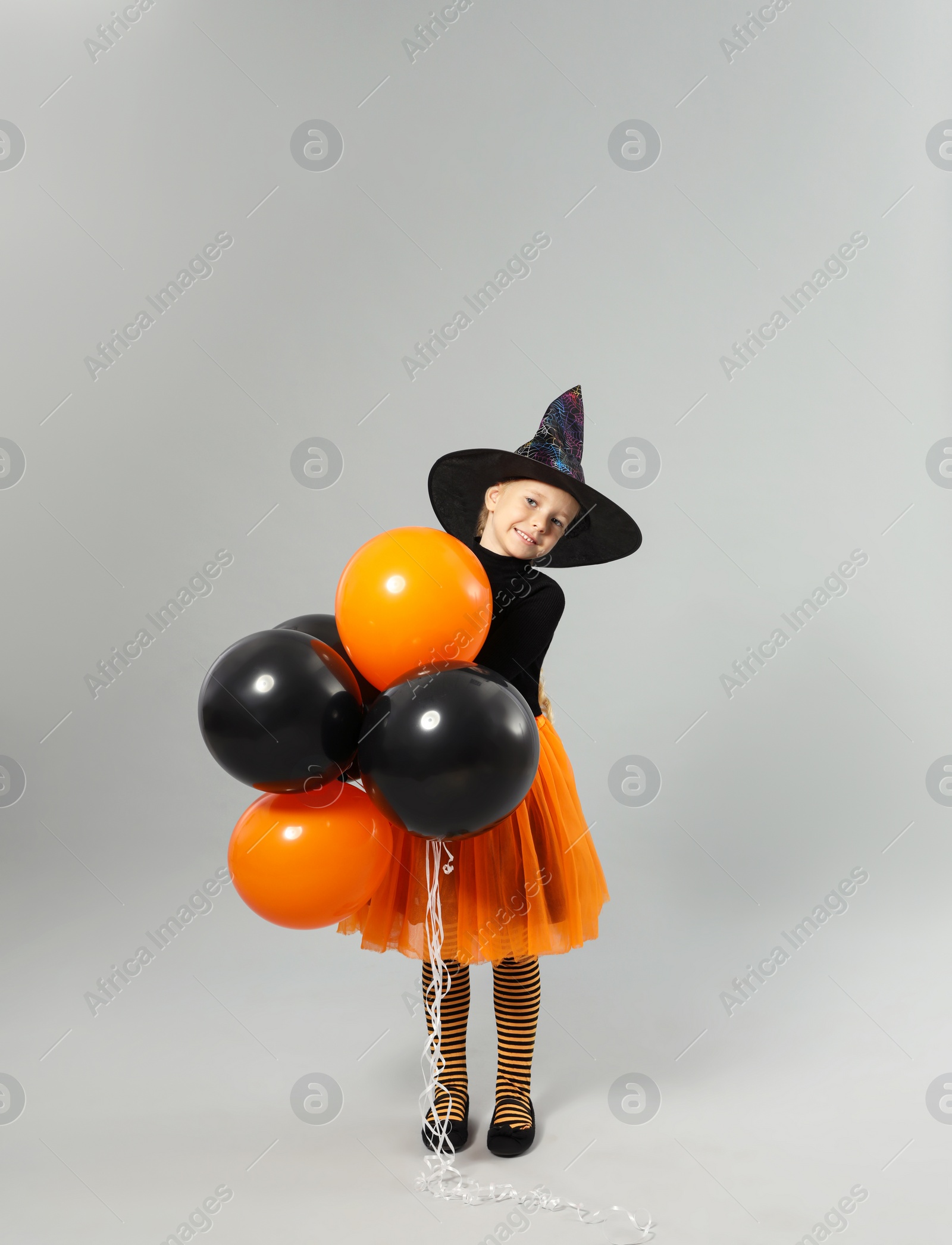 Photo of Cute little girl with balloons wearing Halloween costume on grey background