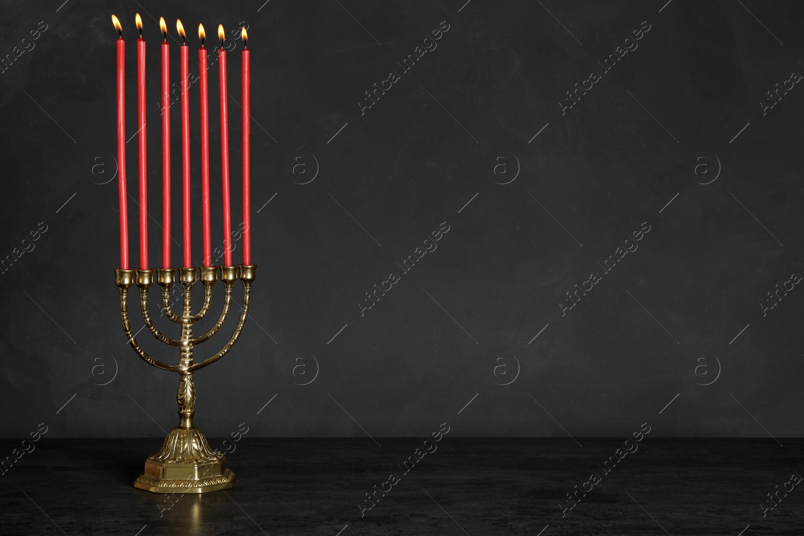 Photo of Golden menorah with burning candles on table against black background, space for text