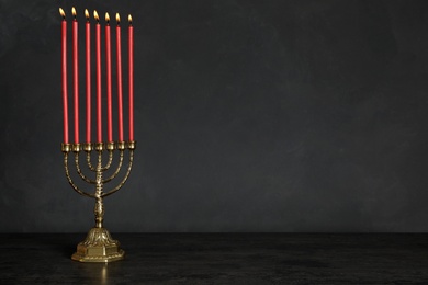 Photo of Golden menorah with burning candles on table against black background, space for text