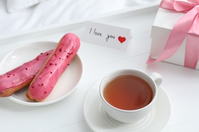 Photo of Tasty breakfast served in bed. Delicious eclairs, tea, gift box and I Love You card on tray