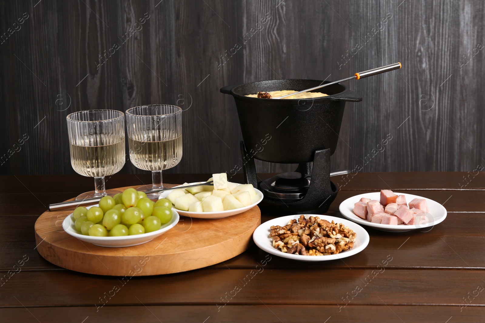 Photo of Fondue pot with tasty melted cheese, forks, wine and different snacks on wooden table