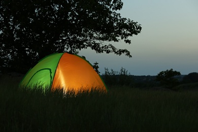 Photo of Modern tent lit from inside in wilderness at night, space for text. Overnight camping