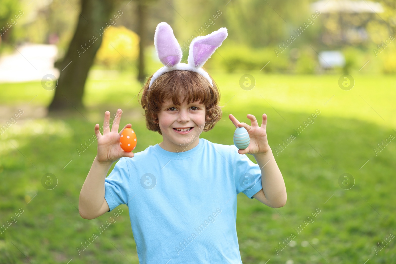Photo of Easter celebration. Cute little boy in bunny ears holding painted eggs outdoors