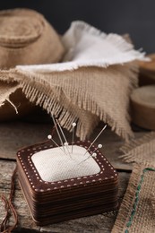 Pincushion, needles and pieces of burlap fabric on wooden table, closeup
