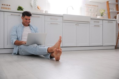 Man with laptop sitting on warm floor in kitchen, space for text. Heating system