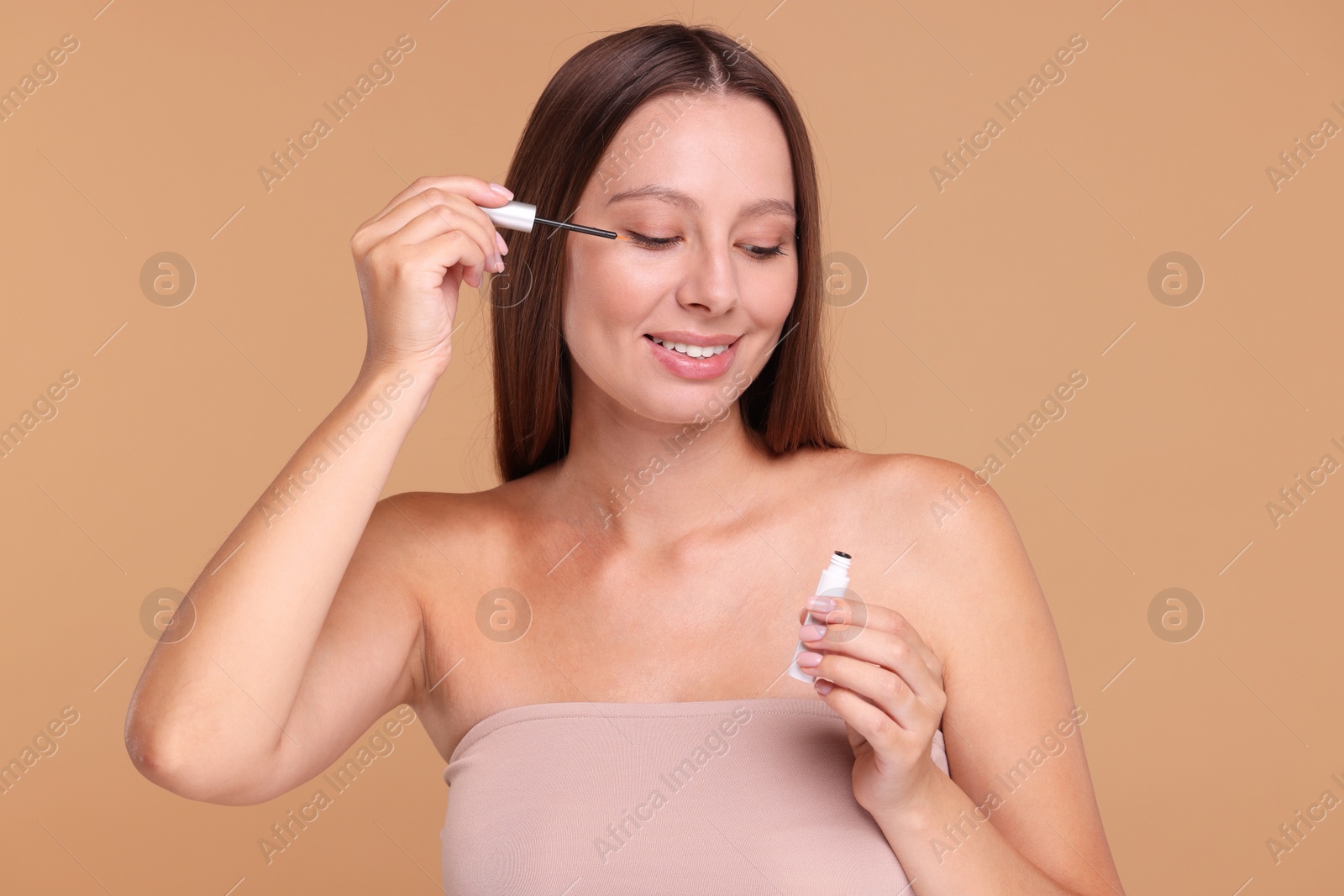 Photo of Beautiful woman applying serum onto eyelashes on beige background