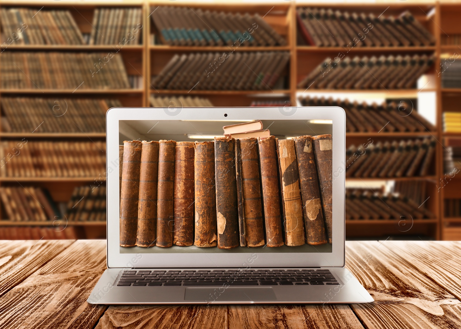 Image of Online library. Modern laptop on wooden table and shelves with books indoors