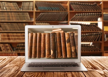 Online library. Modern laptop on wooden table and shelves with books indoors