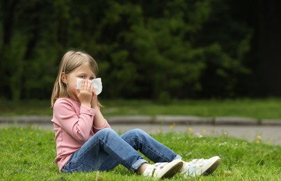 Photo of Little girl suffering from seasonal spring allergy on green grass in park