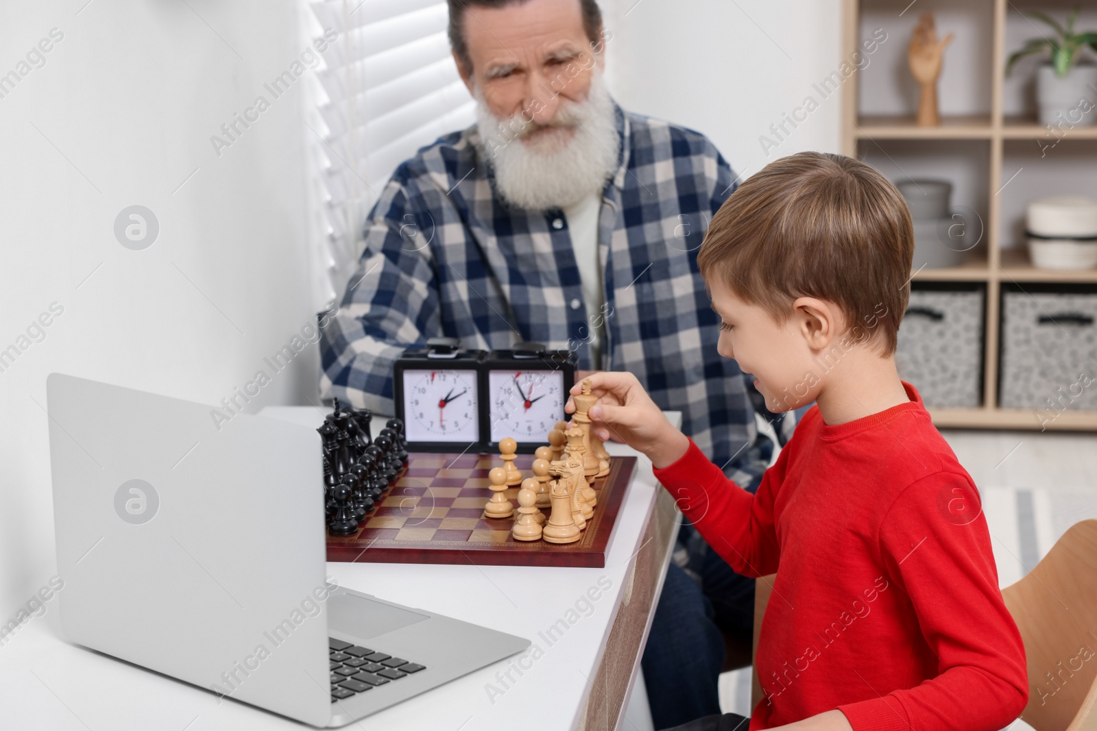 Photo of Grandfather and grandson playing chess following online lesson in room