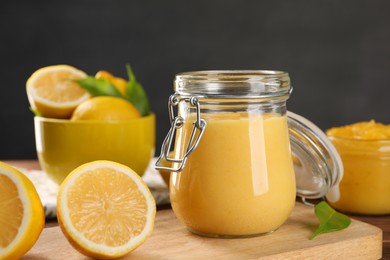 Delicious lemon curd in glass jars, fresh citrus fruits and green leaves on table