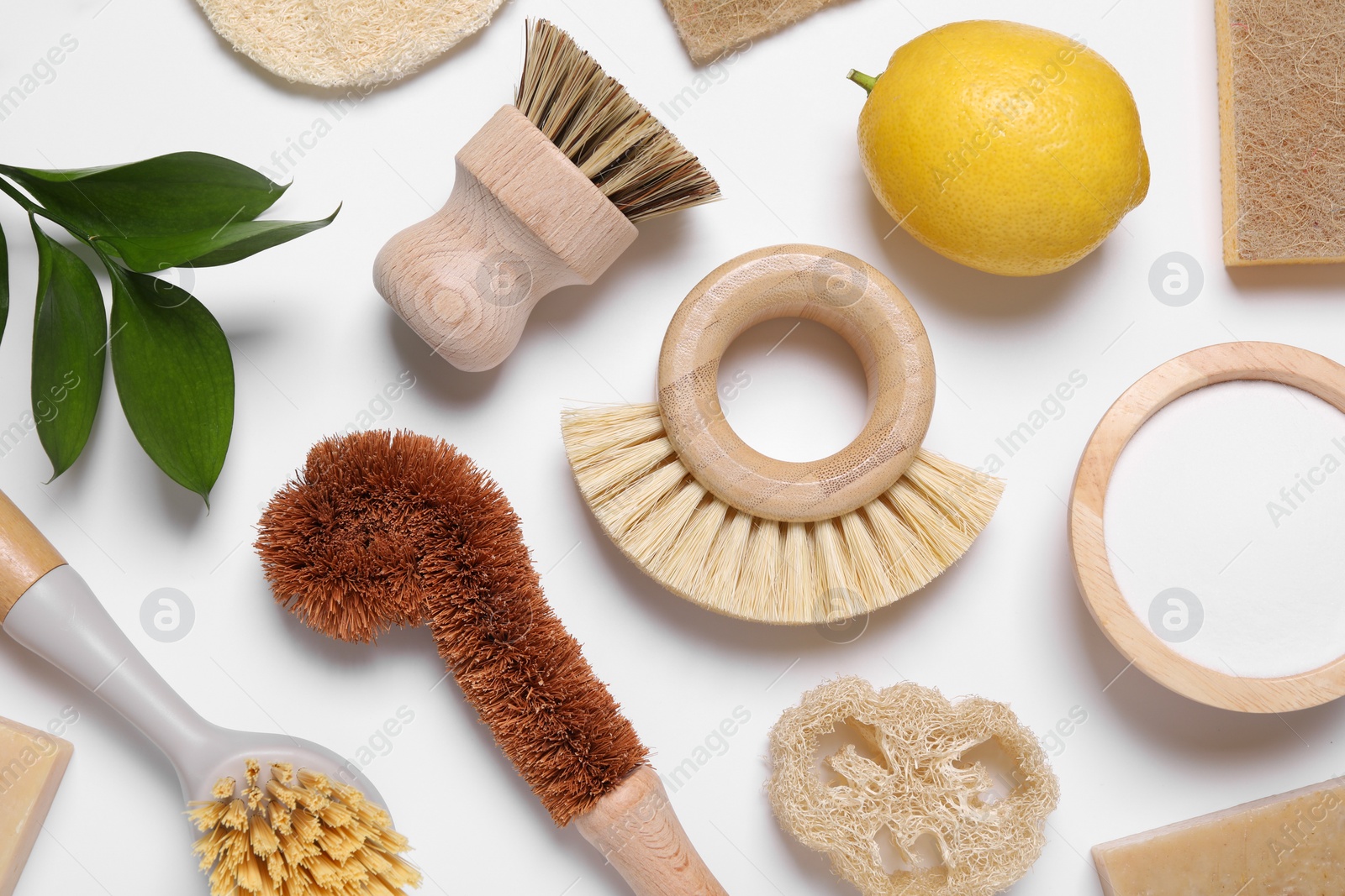 Photo of Cleaning brushes, lemon, baking soda, sponges and floral decor on white background, flat lay