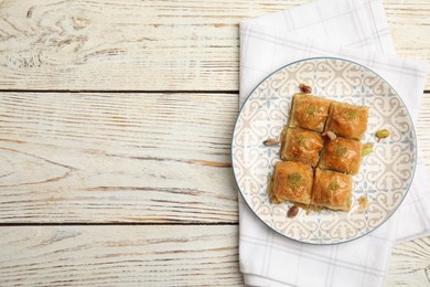 Photo of Delicious baklava with pistachio nuts and napkin on white wooden table, top view. Space for text