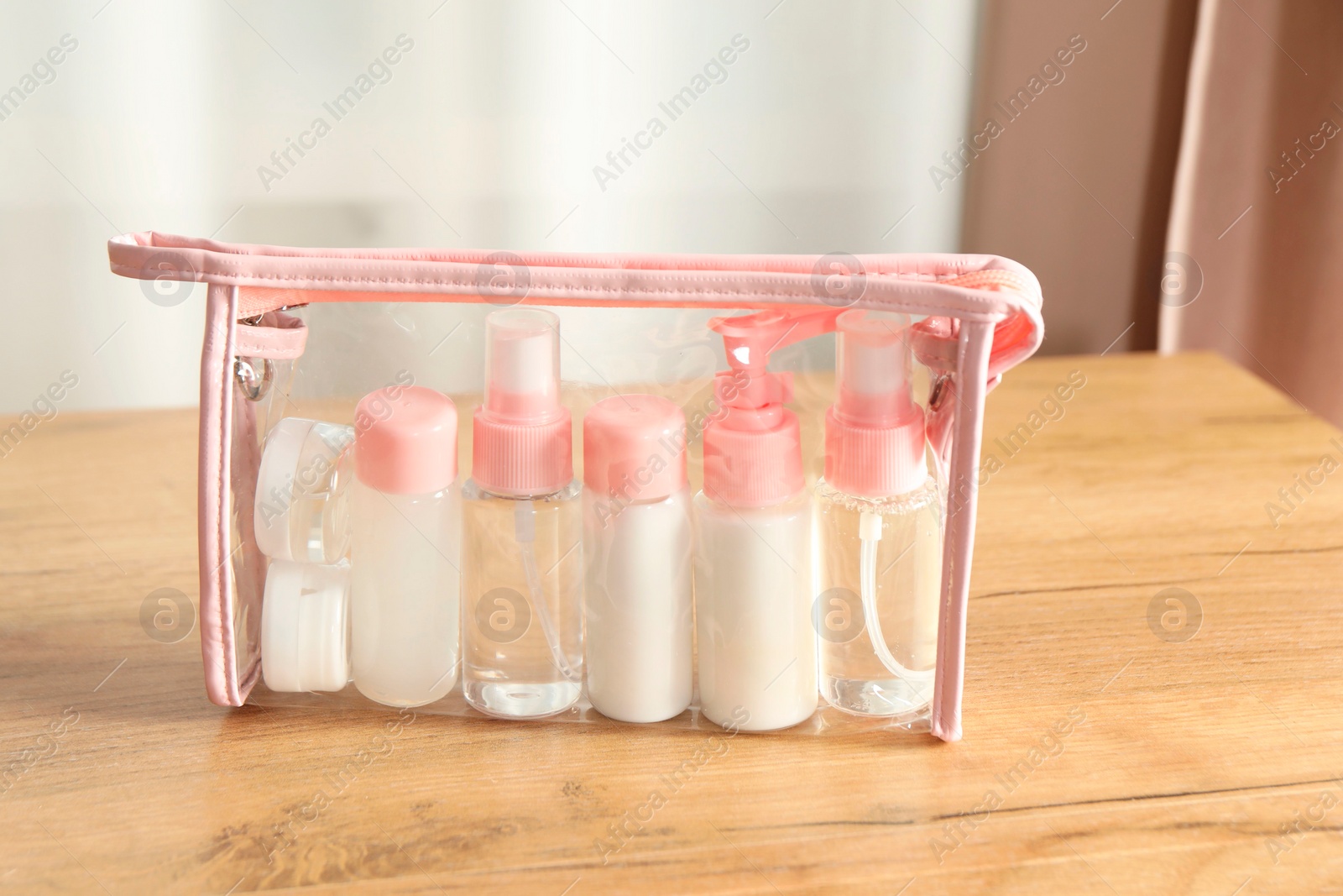 Photo of Cosmetic travel kit. Small containers of personal care products in plastic bag on wooden table indoors