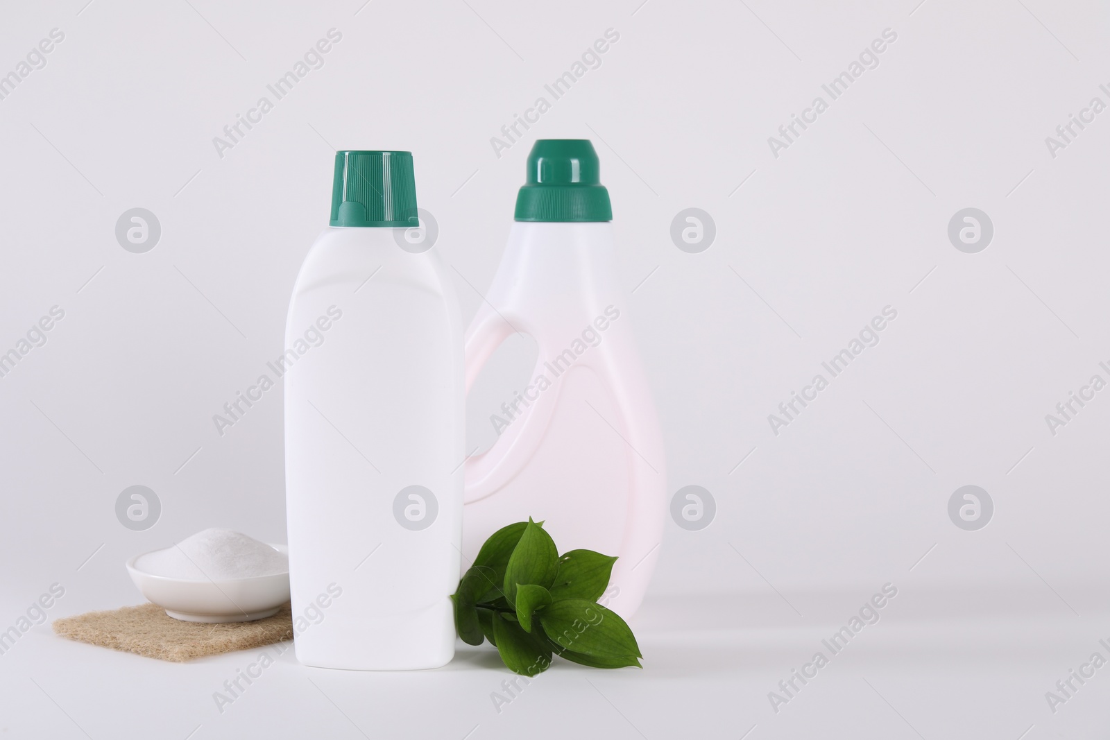 Photo of Bottles of cleaning product, baking soda and green leaves on white background