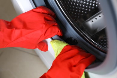 Photo of Woman cleaning washing machine with rag, closeup