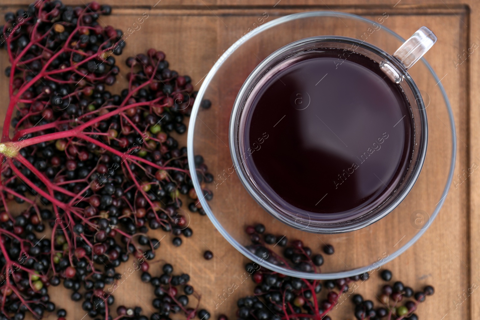 Photo of Glass cup of tasty elderberry tea and Sambucus berries on wooden table, flat lay