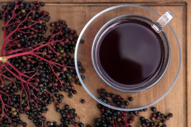 Glass cup of tasty elderberry tea and Sambucus berries on wooden table, flat lay