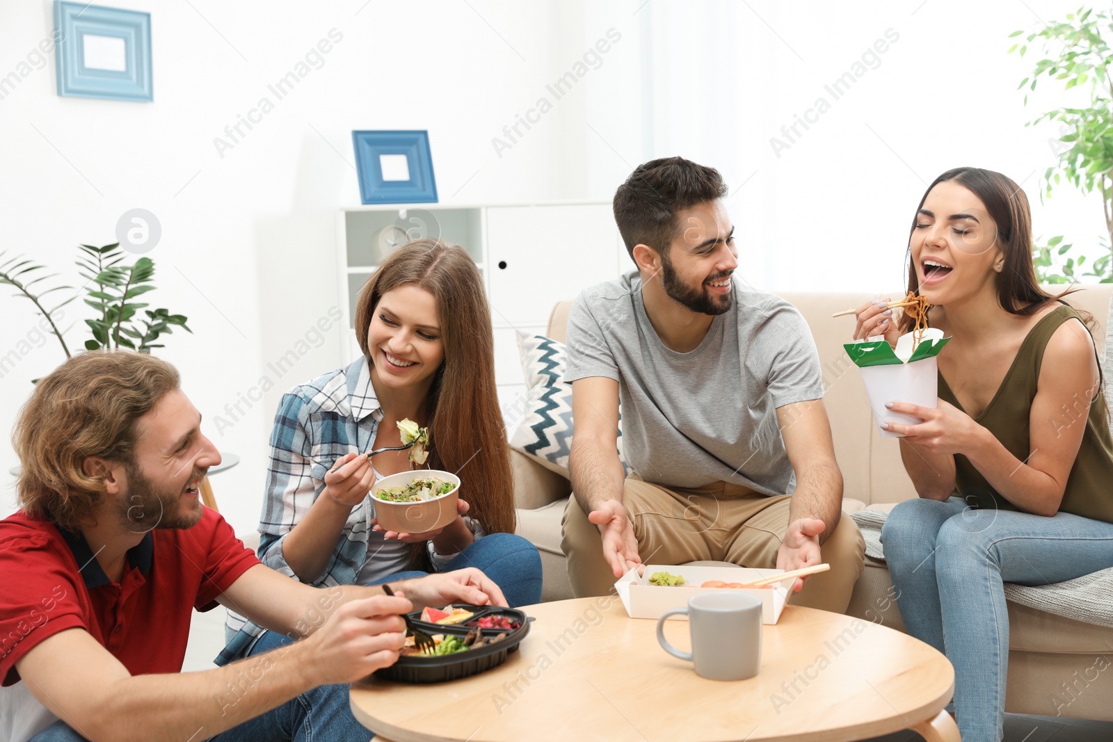 Photo of Young people having lunch together in living room. Food delivery