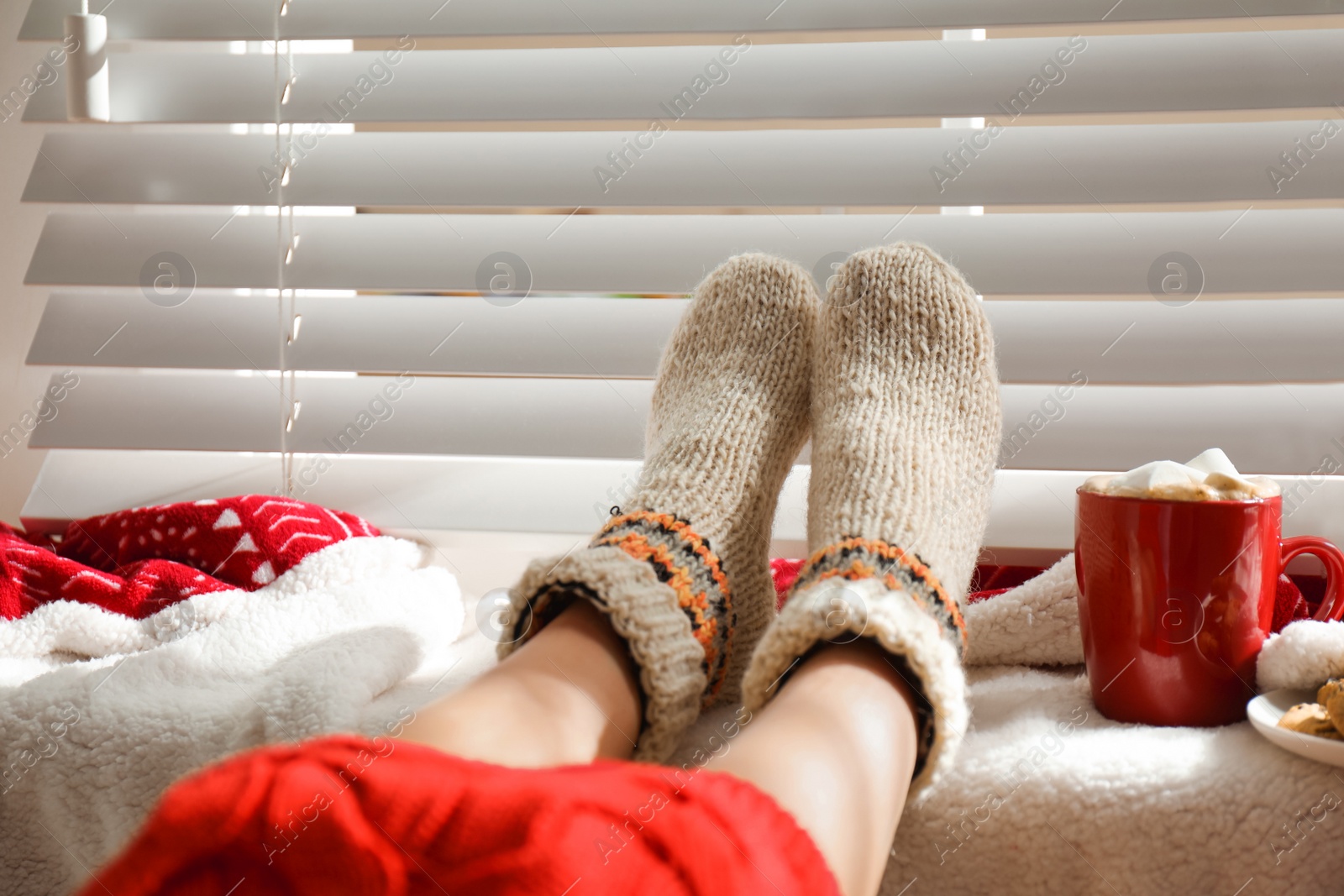 Photo of Woman with cocoa wearing knitted socks at home, closeup. Warm clothes