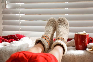 Photo of Woman with cocoa wearing knitted socks at home, closeup. Warm clothes