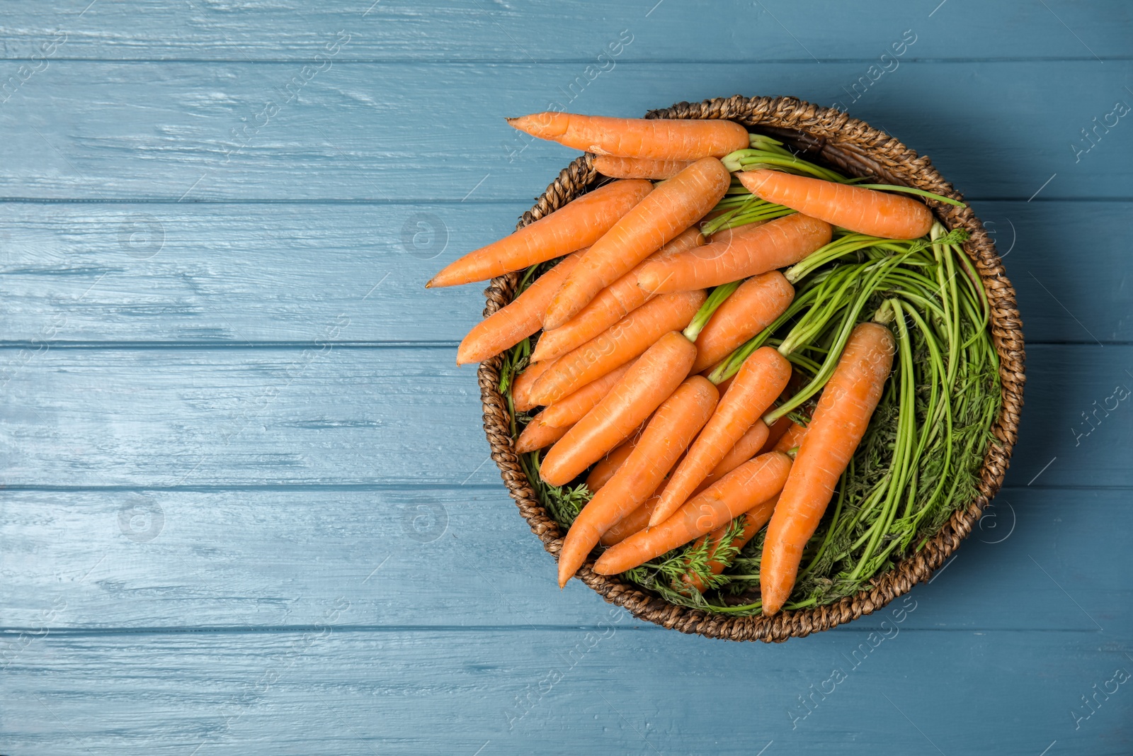 Photo of Bowl with ripe carrots on wooden background, top view