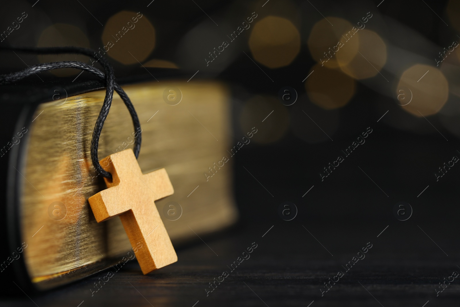 Photo of Christian cross and Bible on black wooden table against blurred background, closeup. Space for text