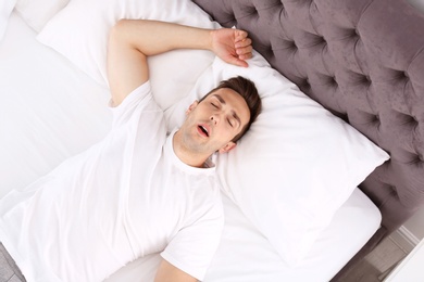 Young man sleeping in bed at home, top view