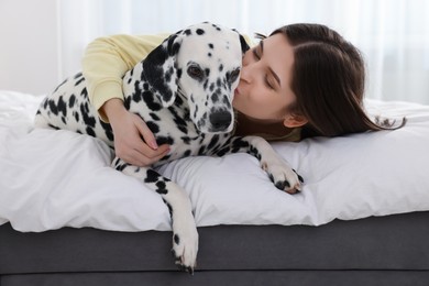 Beautiful woman kissing her adorable Dalmatian dog on bed at home. Lovely pet