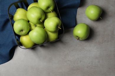 Photo of Black metal container full of apples and napkin on grey table, flat lay. Space for text