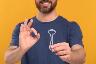 Photo of Man with tongue cleaner showing OK gesture on yellow background, closeup