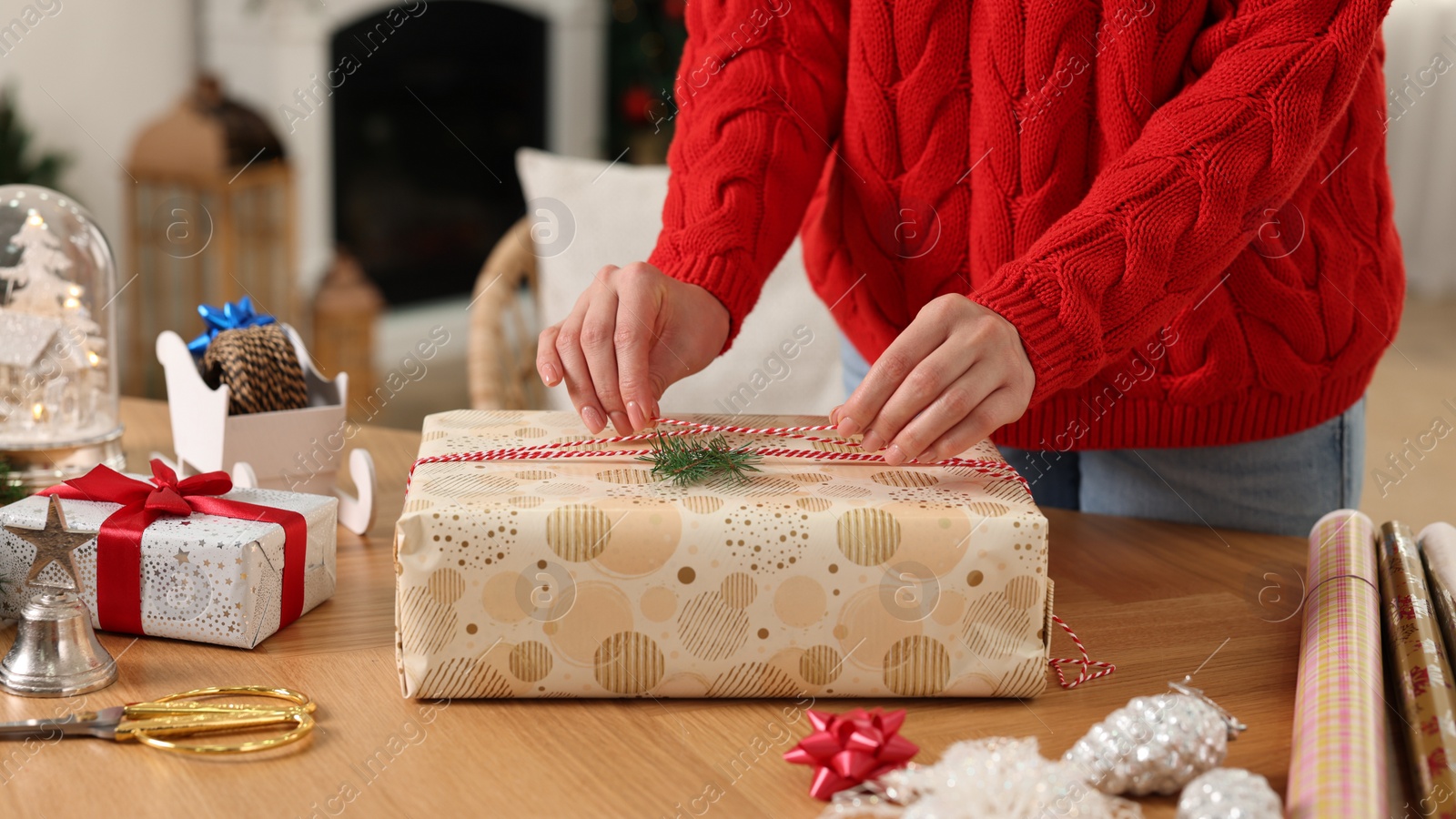 Photo of Woman wrapping Christmas gift at wooden table indoors, closeup