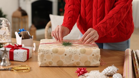 Photo of Woman wrapping Christmas gift at wooden table indoors, closeup