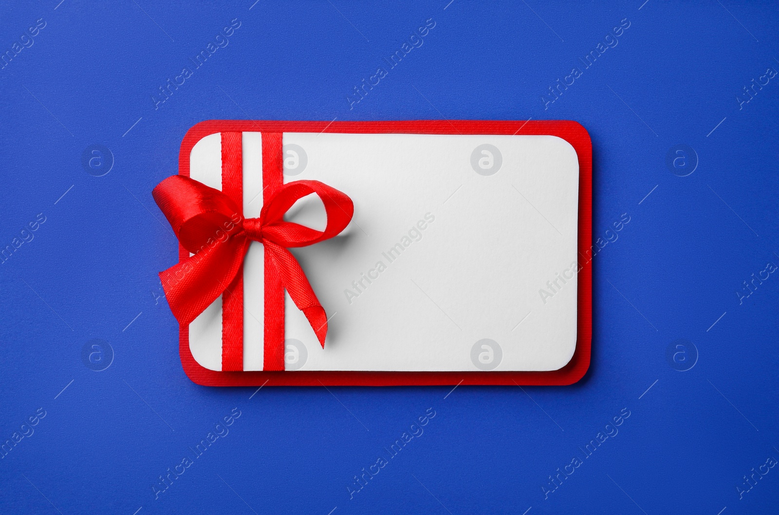 Photo of Blank gift card with red bow on blue background, top view