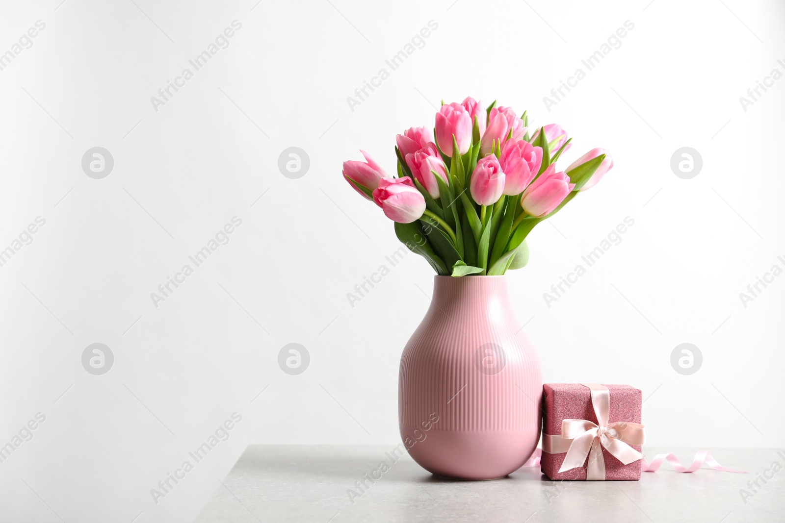 Photo of Bouquet of beautiful spring tulips in vase and gift box on table against white background. International Women's Day